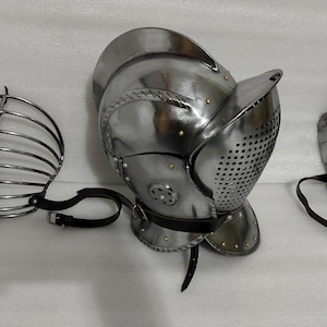 May include: A set of medieval-style armor components, including a helmet with a visor, a face guard, and a shoulder guard. The metal pieces are silver-colored and feature rivets and leather straps.