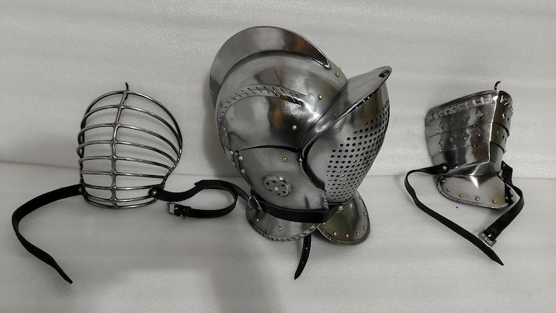 May include: A set of medieval-style armor components, including a helmet with a visor, a face guard, and a shoulder guard. The metal pieces are silver-colored and feature rivets and leather straps.
