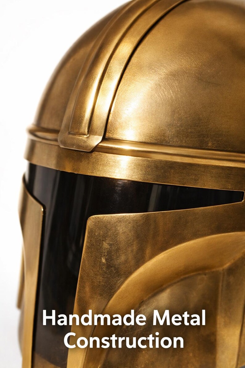 May include: Close-up of a gold-colored metal helmet with a black visor. The helmet has a detailed design with visible seams and edges. The text "Handmade Metal Construction" is displayed on the lower portion of the image.