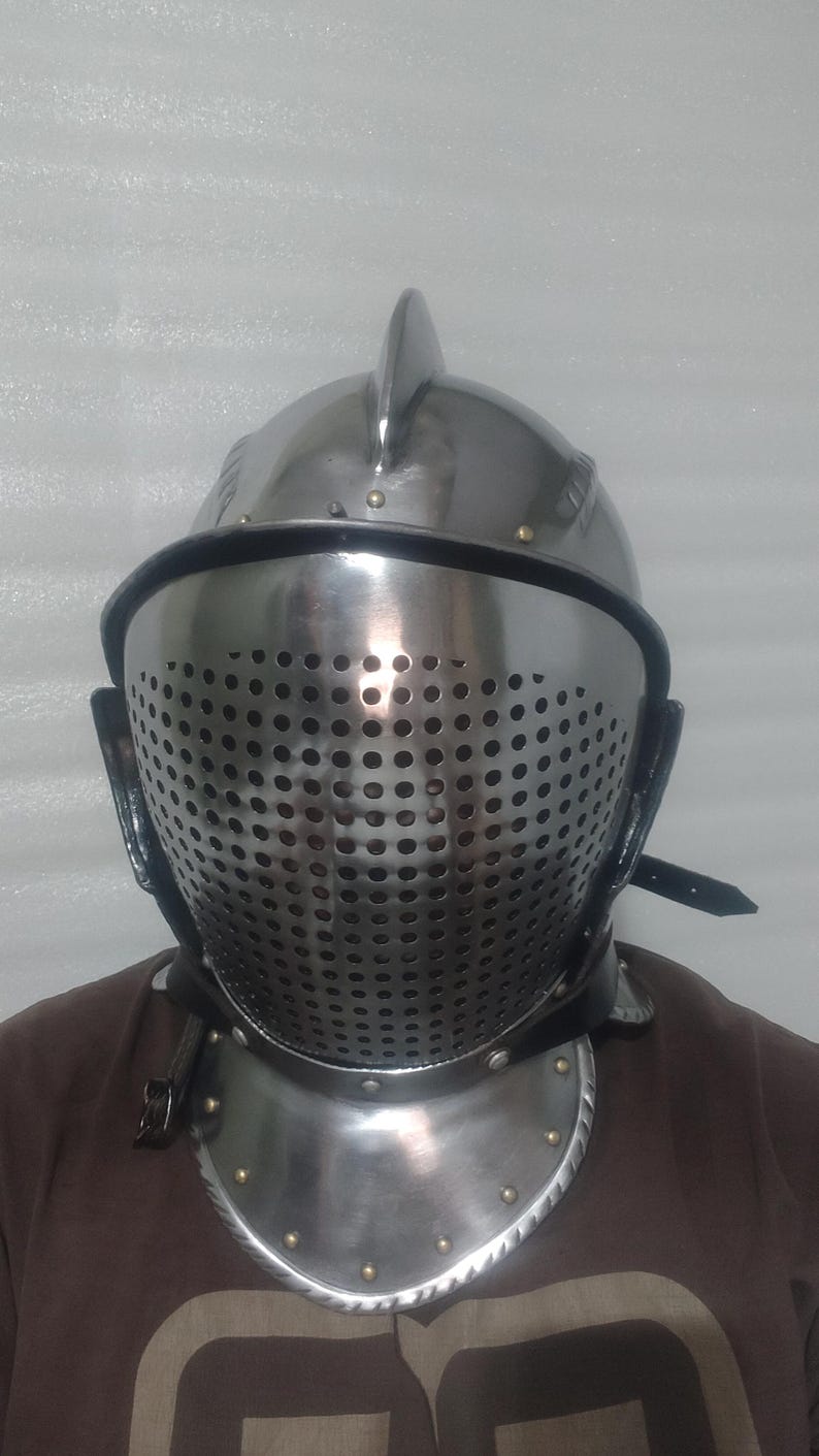 May include: A polished steel knight's helmet with a perforated visor, a prominent central ridge, and a neck guard. The helmet is secured with leather straps and rivets. The overall design suggests medieval armor.
