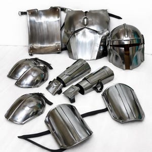 Puede incluir: Un conjunto de piezas de armadura plateadas y brillantes, que incluyen un casco, una placa para el pecho, hombreras y protectores de brazos. La armadura parece estar hecha de metal y est&aacute; dise&ntilde;ada con una est&eacute;tica futurista. Las piezas est&aacute;n dispuestas sobre una superficie blanca.