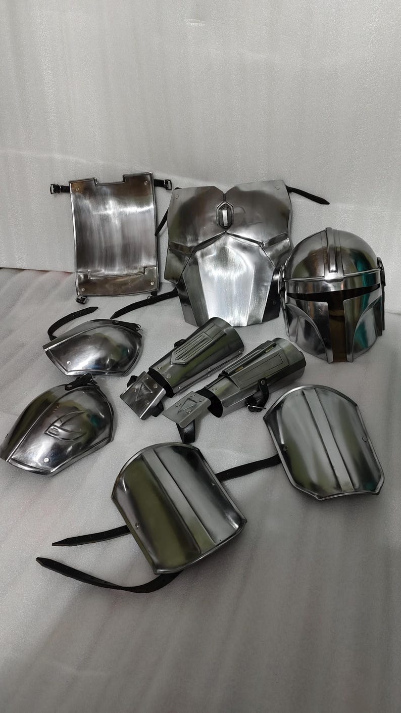 Puede incluir: Un conjunto de piezas de armadura mandaloriana plateada met&aacute;lica, que incluye un casco, una placa para el pecho, hombreras y guanteletes. La armadura tiene un acabado de metal cepillado y se muestra sobre una superficie de color claro. El conjunto est&aacute; dise&ntilde;ado para cosplay o disfraces.
