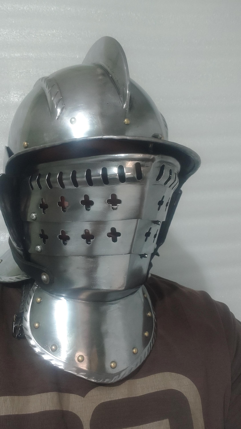 May include: A polished steel helmet with a visor and gorget. The helmet features a rounded top with a crest, a hinged visor with cross-shaped cutouts, and a neck guard. The metal armor is secured with rivets and leather straps.