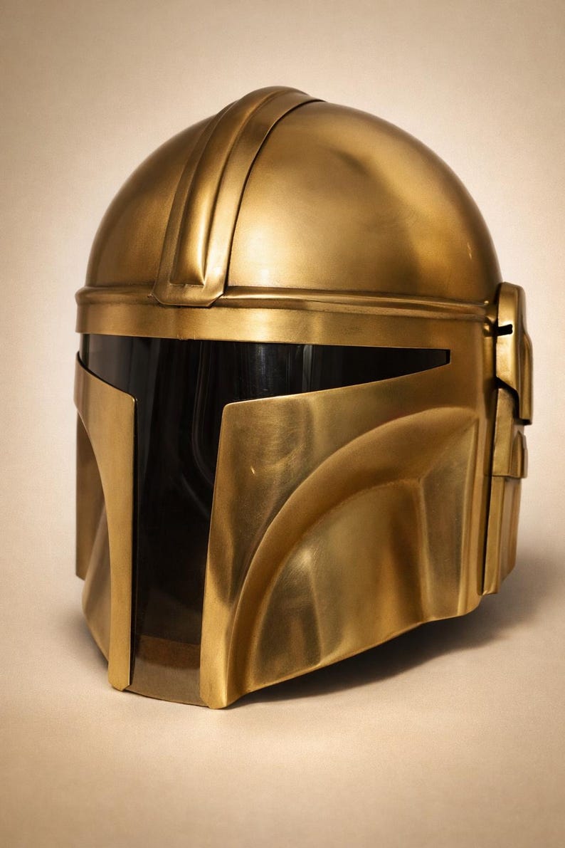 May include: A gold-colored helmet with a sleek, metallic finish. The helmet features a rounded top with a series of ridges and a visor area with a dark, reflective surface. The design includes angular cheek and jaw pieces, suggesting a futuristic or sci-fi theme.