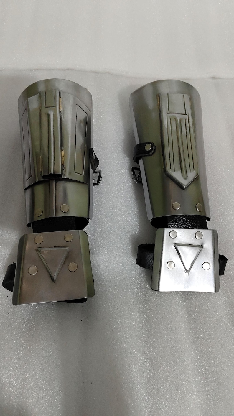 Puede incluir: Dos protectores de brazo plateados con correas de cuero negro. Cada protector tiene un dise&ntilde;o rectangular con formas geom&eacute;tricas y remaches. Los protectores son probablemente para disfraces o cosplay.
