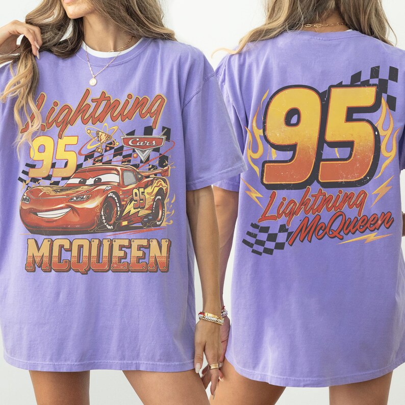 May include: A lilac t-shirt featuring Lightning McQueen from the Cars film. The front graphic shows McQueen with the number 95 and the text "Lightning McQueen" and "McQueen". The back of the shirt has the number 95 and "Lightning McQueen".