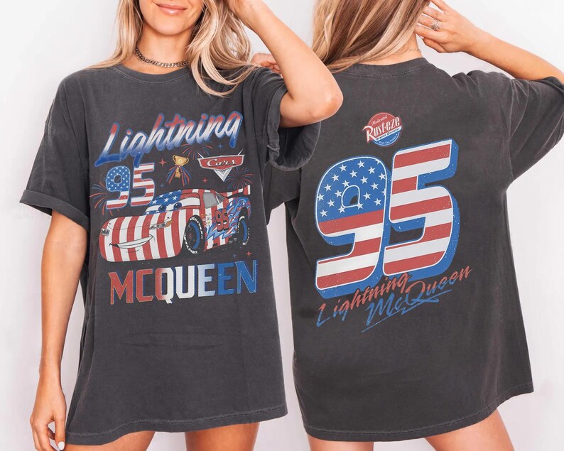 Może przedstawiać: Ciemnoszary t-shirt z kr&oacute;tkim rękawem z grafiką Lightning McQueen w amerykański wz&oacute;r flagi. Z przodu znajduje się napis Lightning McQueen i 95. Z tyłu widnieje duża liczba 95 z pasami flagi oraz logo Rust-eze.
