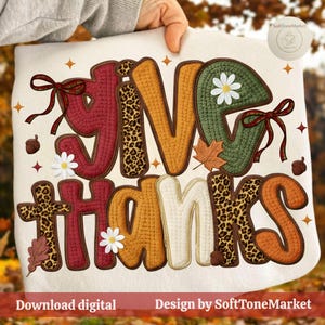 Può includere: Un tessuto color crema con le parole "GIVE THANKS" in un design a tema autunnale. Le lettere sono in vari colori e motivi, tra cui stampa leopardata, con accenti floreali e di foglie. Il testo "Download digital" e "Design by SoftToneMarket" sono anch'essi visibili.