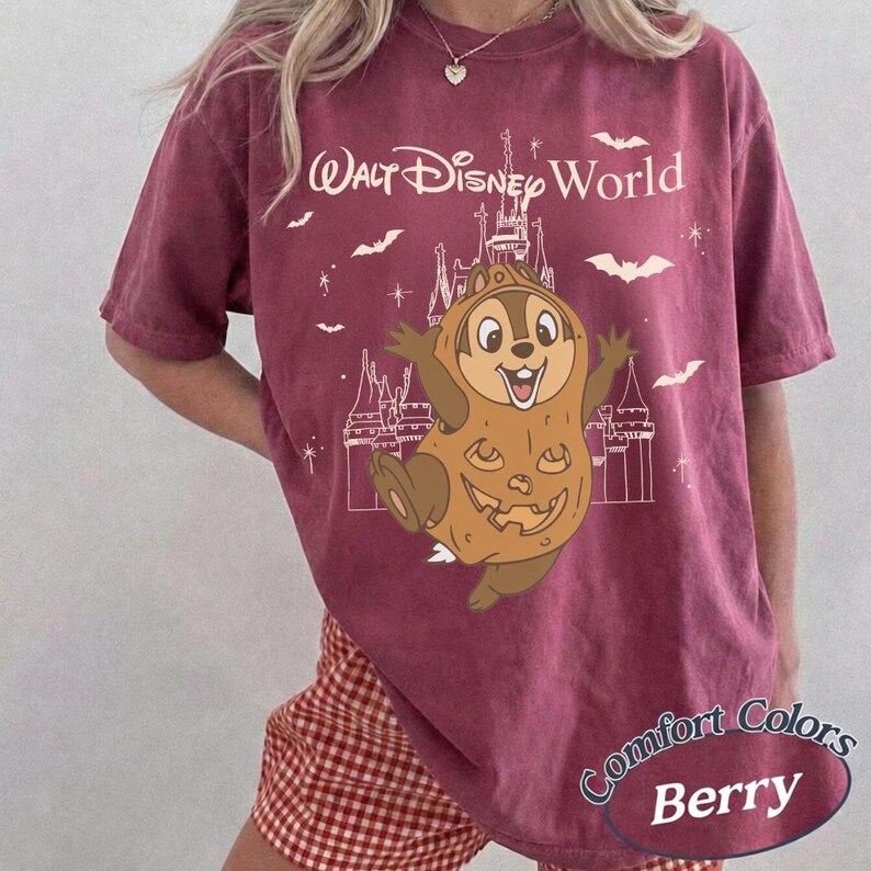 May include: A berry-coloured t-shirt featuring a graphic of Chip from Disney's Chip 'n Dale Rescue Rangers dressed as a jack-o'-lantern, with the text "Walt Disney World." The shirt also features bats and a castle design. The words "Comfort Colors" and "Berry" are also printed.