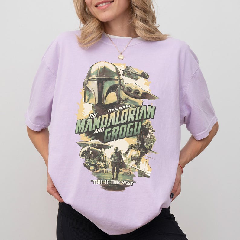 K&ouml;nnte beinhalten: Ein helllila T-Shirt mit einem Star Wars-Motiv. Das Design zeigt den Text "The Mandalorian and Grogu" zusammen mit Bildern des Mandalorianers, Grogu und anderer Charaktere. Der Satz "THIS IS THE WAY" ist ebenfalls auf dem Shirt aufgedruckt.
