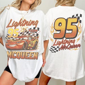 May include: White t-shirt with a graphic of Lightning McQueen from the Cars film. The front design includes McQueen, the number 95, and a checkered flag. The back features a large "95" and the words "Lightning McQueen".