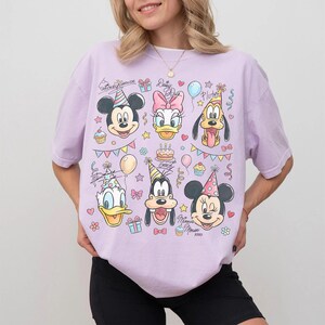 Puede incluir: Camiseta lila claro con un gr&aacute;fico colorido de Mickey Mouse, Daisy Duck, Donald Duck, Goofy, Pluto y Minnie Mouse, todos con sombreros de fiesta. El dise&ntilde;o incluye pastel de cumplea&ntilde;os, globos y confeti.