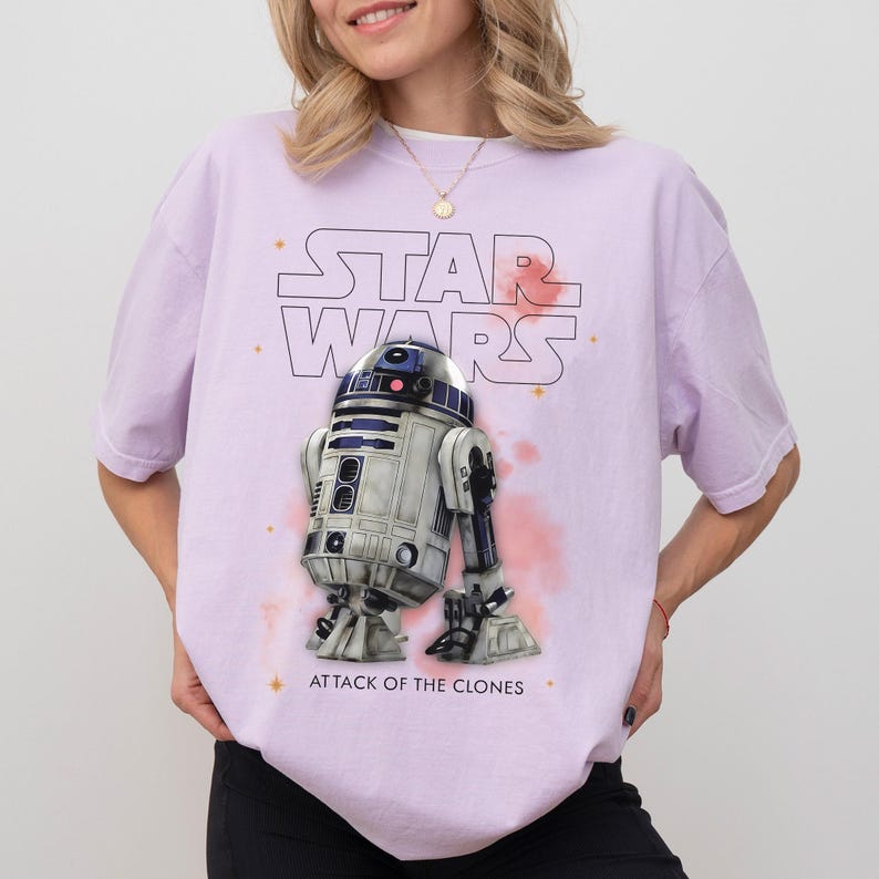 Peut inclure: T-shirt lilas avec le logo Star Wars et une image de R2-D2. Le texte "ATTACK OF THE CLONES" est imprim&eacute; en dessous du dro&iuml;de. Le t-shirt a des manches courtes et une coupe d&eacute;contract&eacute;e.