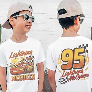 May include: White t-shirt featuring Lightning McQueen from the Cars movie. The front of the shirt displays the character with the text "Lightning 95 McQueen". The back of the shirt has a large "95" with flames and the text "Lightning McQueen".