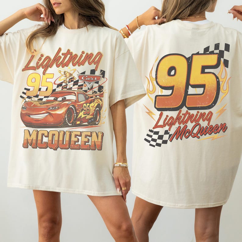 May include: Cream-coloured t-shirt featuring a graphic of Lightning McQueen from the Cars movie. The front displays the character with the text "Lightning 95 McQueen". The back of the shirt has a large "95" with flames and the text "Lightning McQueen".