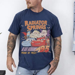 May include: Navy blue t-shirt featuring a graphic of characters from the movie Cars, with the text "Radiator Springs" and "Trunk or Treat". The graphic includes the number "95".