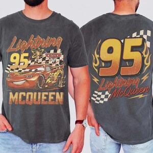 May include: Dark grey t-shirt featuring Lightning McQueen from the Cars film. The front graphic shows McQueen with the number 95 and the text "Lightning McQueen" and "Cars". The back has a large "95" with flames and the text "Lightning McQueen".
