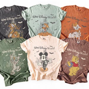 May include: Six vintage-style t-shirts in various colours, each featuring a Disney character in a Halloween costume with the text "Walt Disney World". The shirts are in shades of grey, green, orange, and beige.
