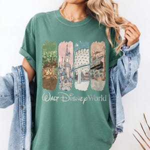 May include: A teal-colored t-shirt featuring a graphic of Walt Disney World landmarks. The design includes images of a castle, Spaceship Earth, and other attractions. The words "Walt Disney World" are printed in a script font below the images.