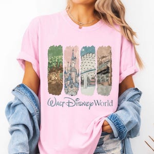 May include: Pink t-shirt featuring a graphic of Walt Disney World landmarks. The design includes images of the Tree of Life, Cinderella Castle, Spaceship Earth, and the World Showcase. The words "Walt Disney World" are printed in a light blue script font.