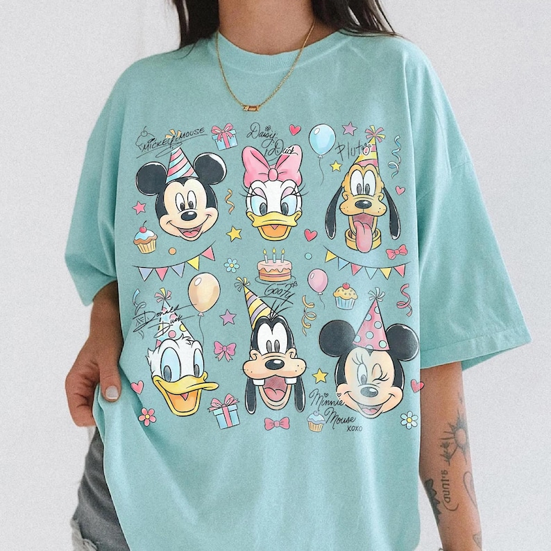 Puede incluir: Una camiseta azul claro con los personajes de dibujos animados Mickey Mouse, Daisy Duck, Pluto, Donald Duck, Goofy y Minnie Mouse. El dise&ntilde;o incluye gorros de fiesta, globos y el texto "Mickey Mouse" y "Daisy Duck".