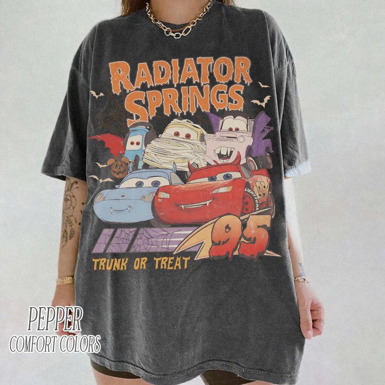 May include: Dark gray t-shirt featuring a graphic of characters from the movie Cars, with the text "Radiator Springs" and "Trunk or Treat". The graphic includes the number "95". The shirt is from Pepper Comfort Colors.
