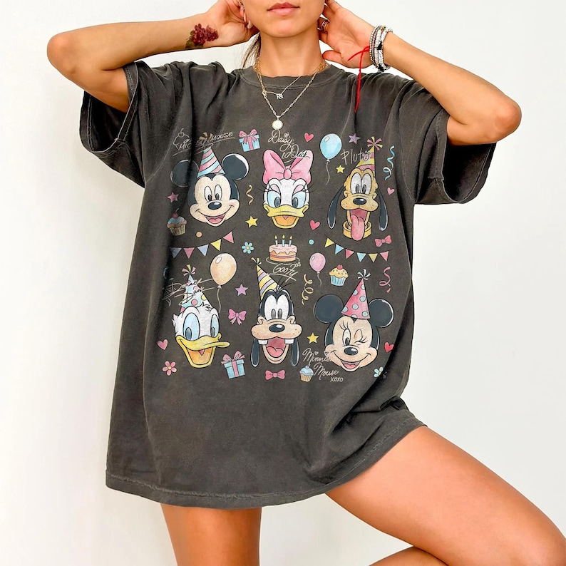 Puede incluir: Camiseta gris oscuro con un gr&aacute;fico colorido de Mickey Mouse, Minnie Mouse, Donald Duck, Daisy Duck, Goofy y Pluto. El dise&ntilde;o incluye elementos de fiesta de cumplea&ntilde;os como globos, cupcakes y una tarta. La camiseta tiene un corte holgado.