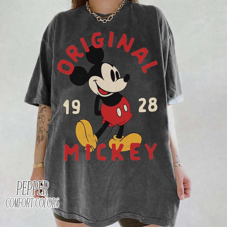 May include: Dark gray t-shirt featuring a vintage Mickey Mouse graphic. The design includes the words "ORIGINAL MICKEY" in red, with the year "1928". The shirt is from the brand "PEPPER COMFORT COLORS".
