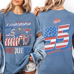 Może przedstawiać: Niebieski t-shirt z grafiką samochodu wyścigowego w barwach flagi amerykańskiej, numerem 95 i napisem Lightning McQueen z przodu. Z tyłu znajduje się duży numer 95 w paski flagi amerykańskiej oraz logo Rust-eze w g&oacute;rnej części koszulki.
