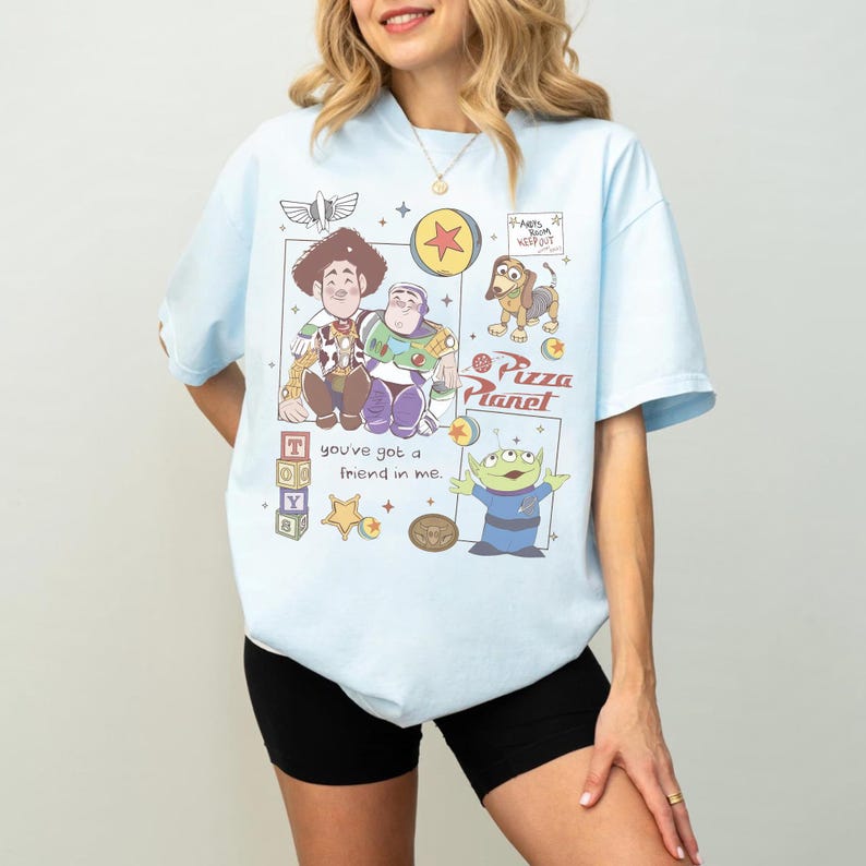 Pu&ograve; includere: T-shirt azzurra con una grafica colorata dei personaggi di Toy Story, tra cui Woody, Buzz Lightyear e gli omini verdi. La maglietta presenta anche la scritta "Pizza Planet" e "You've got a friend in me."