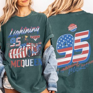 Może przedstawiać: Ciemnozielono-niebieski t-shirt z grafiką przedstawiającą Lightning McQueen z filmu Cars z przodu oraz napisem Lightning McQueen i 95. Z tyłu znajduje się duża liczba 95 w barwach flagi USA, logo Rust-eze oraz napis Lightning McQueen.