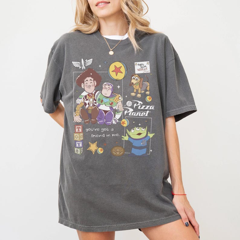 Pu&ograve; includere: T-shirt grigio scuro con una grafica dei personaggi del film Toy Story, tra cui Woody, Buzz Lightyear e gli omini verdi. La maglietta presenta anche il testo "Pizza Planet" e "You've got a friend in me."