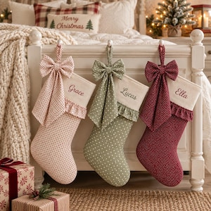 May include: Three Christmas stockings featuring polka dot patterns in light pink, sage green, and deep red. Each stocking has a cream-coloured cuff embroidered with the names Grace, Lucas, and Ella, finished with a matching fabric bow and ruffle.