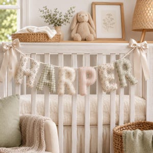 May include: A decorative fabric banner spelling the name HARPER in plush, stuffed letters. Each letter features a different pattern, including floral prints, gingham checks, and vertical stripes in soft shades of sage green, cream, and blush pink.