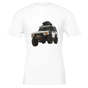 Puede incluir: Camiseta blanca con una ilustración de dibujos animados de un vehículo todoterreno Land Rover. El vehículo es blanco con detalles en negro, neumáticos grandes y una baca. Las palabras "LAND ROVER" están impresas en la parte delantera.