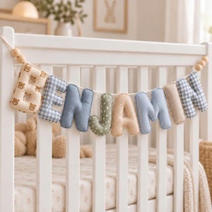 May include: A decorative fabric banner spelling the name BENJAMIN with individual stuffed letters. The letters feature various patterns including teddy bears, blue gingham, solid blue, green with white stars, beige polka dots, and blue stripes.