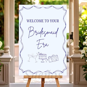 Pode incluir: Uma placa branca em um cavalete de madeira com o texto "WELCOME TO YOUR Bridesmaid Era" em escrita azul escuro. A placa é emoldurada com uma borda decorativa azul escuro e apresenta ilustrações de taças de champanhe, um bolo e uma câmera.