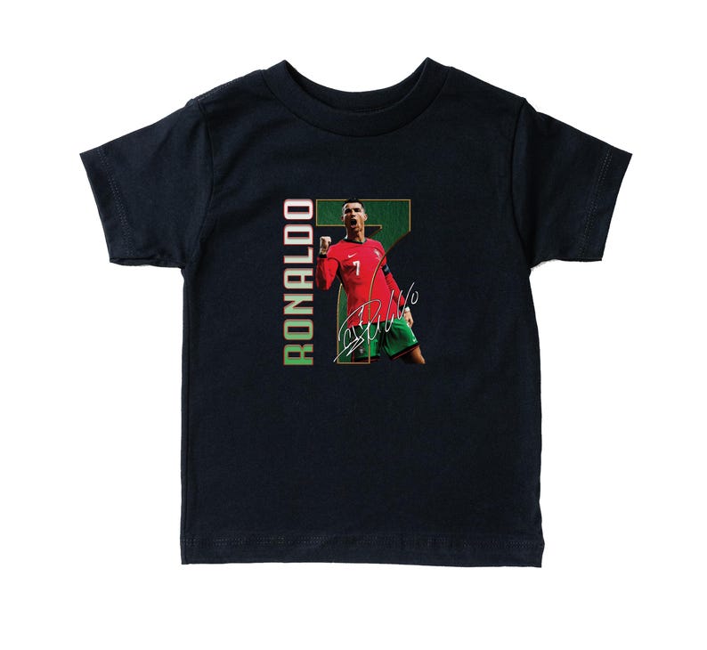 Puede incluir: Camiseta azul marino para ni&ntilde;os peque&ntilde;os con un gr&aacute;fico de un jugador de f&uacute;tbol con una camiseta roja con el n&uacute;mero 7. La camiseta tiene el nombre "RONALDO" impreso verticalmente en verde y blanco, junto con la firma del jugador.