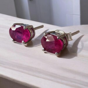 K&ouml;nnte beinhalten: Ein Paar Ohrstecker mit oval geschliffenen, tiefrosa Edelsteinen, gefasst in silberfarbenem Metall. Die Ohrringe haben ein klassisches Design mit Stecker und Verschluss. Die Edelsteine sind der Blickfang und zeigen ihre lebendige Farbe.