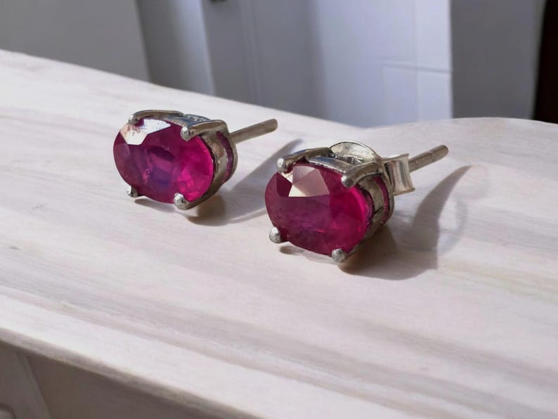 K&ouml;nnte beinhalten: Ein Paar Ohrstecker mit oval geschliffenen, tiefrosa Edelsteinen, gefasst in silberfarbenem Metall. Die Ohrringe haben ein klassisches Design mit Stecker und Verschluss. Die Edelsteine sind der Blickfang und zeigen ihre lebendige Farbe.