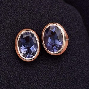 Peut inclure: Une paire de boucles d'oreilles à clous de forme ovale. Chaque boucle d'oreille présente une pierre précieuse bleu foncé facettée sertie dans une lunette de couleur or rose. Les boucles d'oreilles sont présentées sur un fond en tissu bleu marine foncé.
