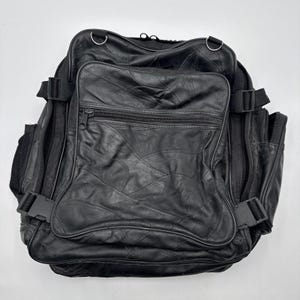 May include: A black leather backpack featuring a patchwork design with multiple zippered compartments, side pockets, and adjustable black nylon straps with plastic buckles. The exterior is constructed from various stitched leather pieces.