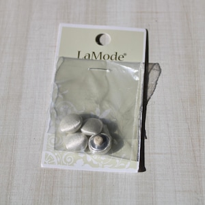 May include: A package of four silver heart-shaped buttons with a black button in the center. The package is labeled "LaMode".