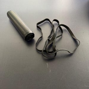 May include: A black roll of plastic trash bags and several black rubber bands are on a dark surface. The bags are cylindrical and tightly rolled. The rubber bands are looped and scattered.
