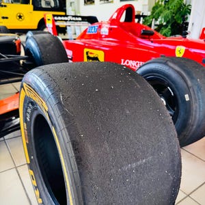 May include: A bright red Formula One race car featuring a prominent black Pirelli P Zero slick tire in the foreground. The car body displays yellow and black logos, including a prancing horse emblem, and the text LONGINES on the side panel.