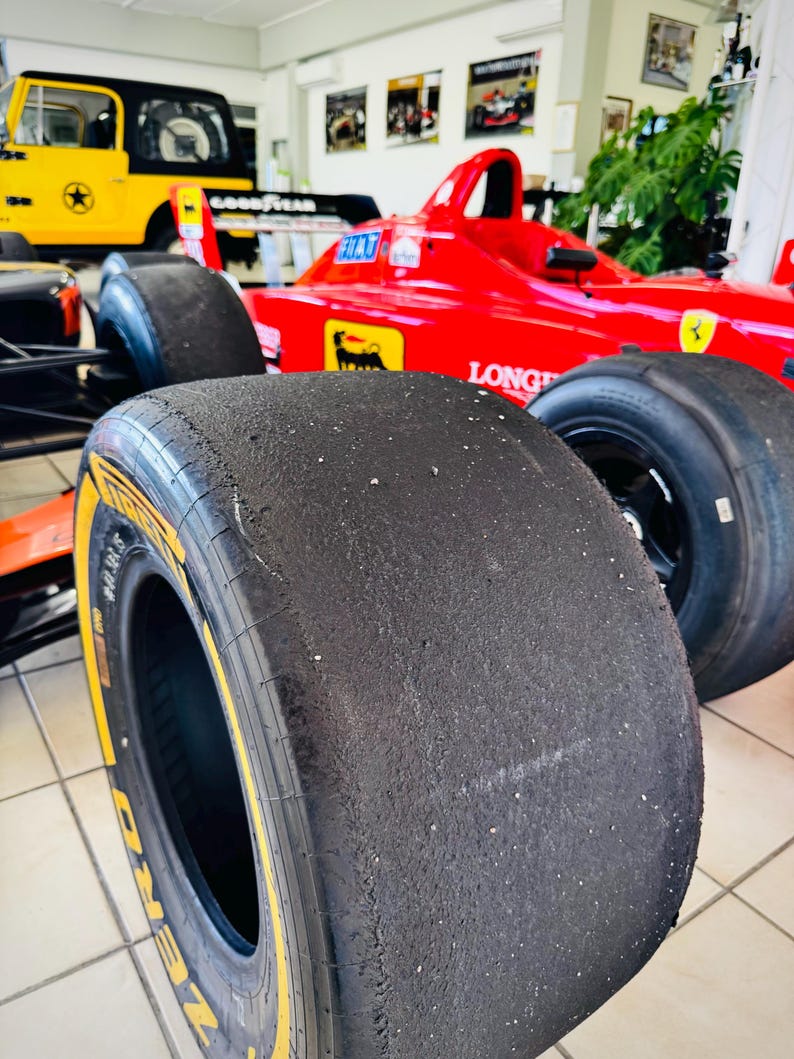May include: A bright red Formula One race car featuring a prominent black Pirelli P Zero slick tire in the foreground. The car body displays yellow and black logos, including a prancing horse emblem, and the text LONGINES on the side panel.
