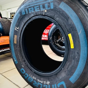 May include: A black Pirelli Cinturato wet racing tire featuring blue lettering on the sidewall. The tire is marked with FL, #18 BAR WET4, and a yellow Driver Academy sticker. The text 305/680-18 is visible on the side of the rubber tire casing.