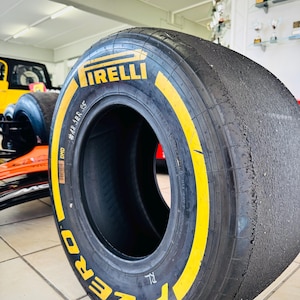 May include: A black Pirelli P Zero racing slick tire with yellow branding on the sidewall. The tire features a smooth, worn tread surface and includes the text Pirelli, P Zero, DMD, and #48 JER S5 printed clearly on the side of the rubber casing.