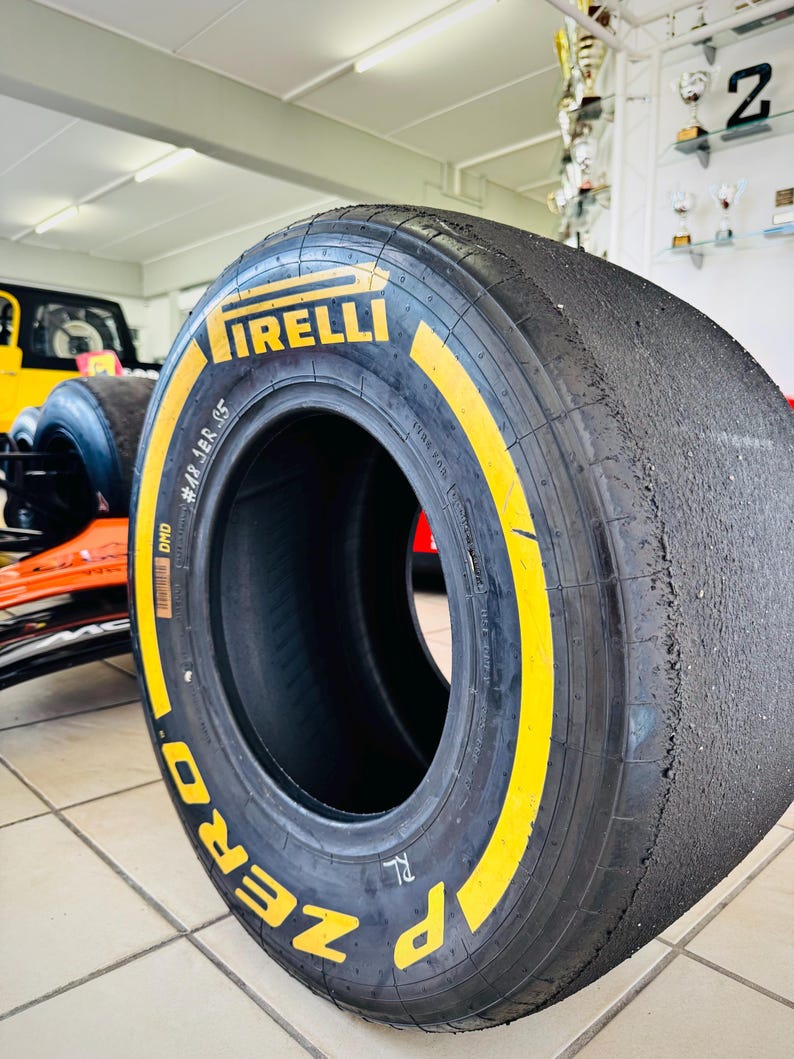 May include: A black Pirelli P Zero racing slick tire with yellow branding on the sidewall. The tire features a smooth, worn tread surface and includes the text Pirelli, P Zero, DMD, and #48 JER S5 printed clearly on the side of the rubber casing.
