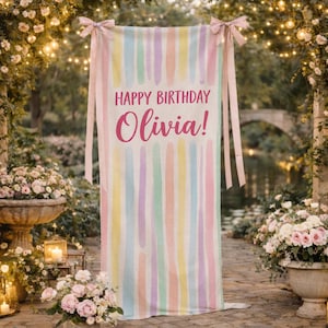 May include: A pastel-colored birthday banner with vertical brushstroke stripes in shades of pink, yellow, blue, and green. The banner reads "HAPPY BIRTHDAY Olivia!" in a pink script font, and is tied with pink ribbons.